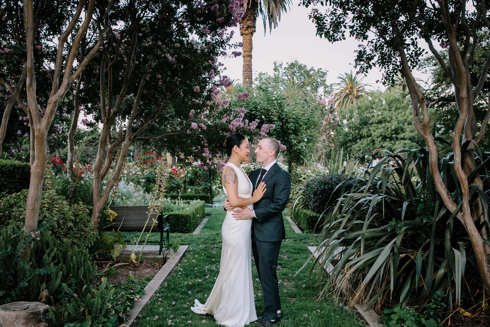 Bride and groom holding each other and smiling at each other in a garden.