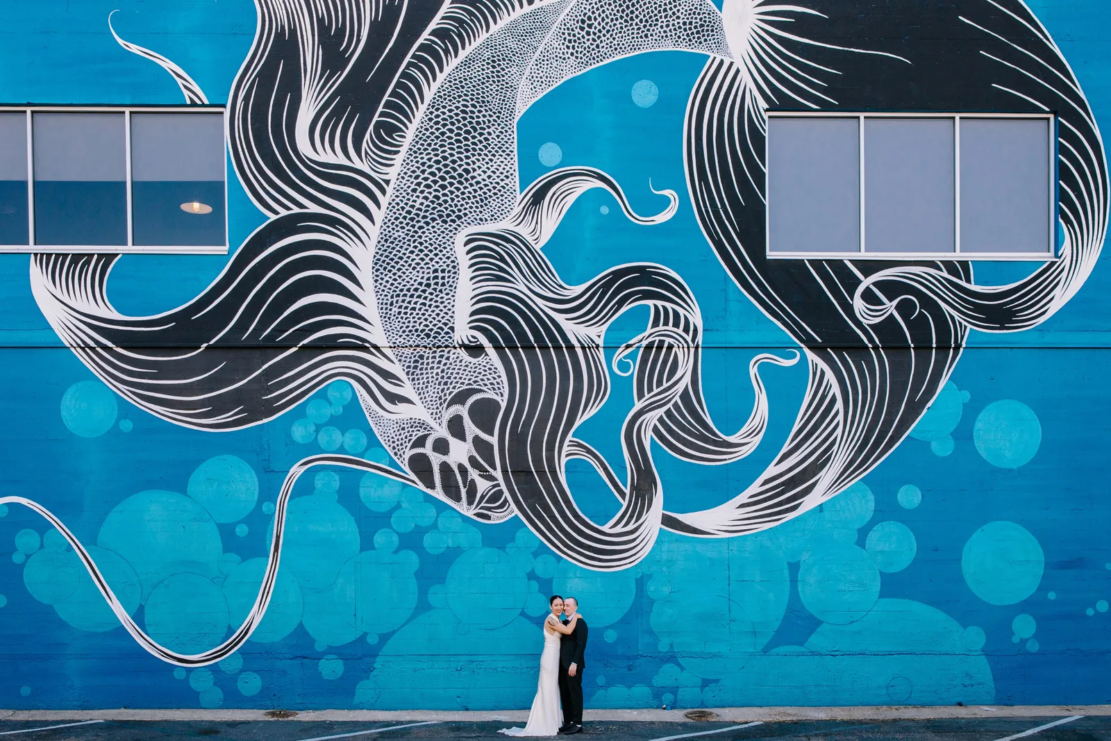 Bride and groom embracing in front of a large blue mural.