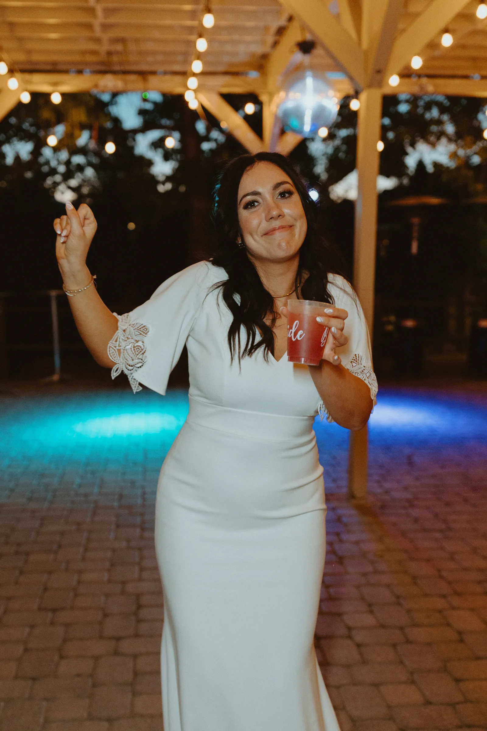 Bride dancing and smiling with a drink in her hand.