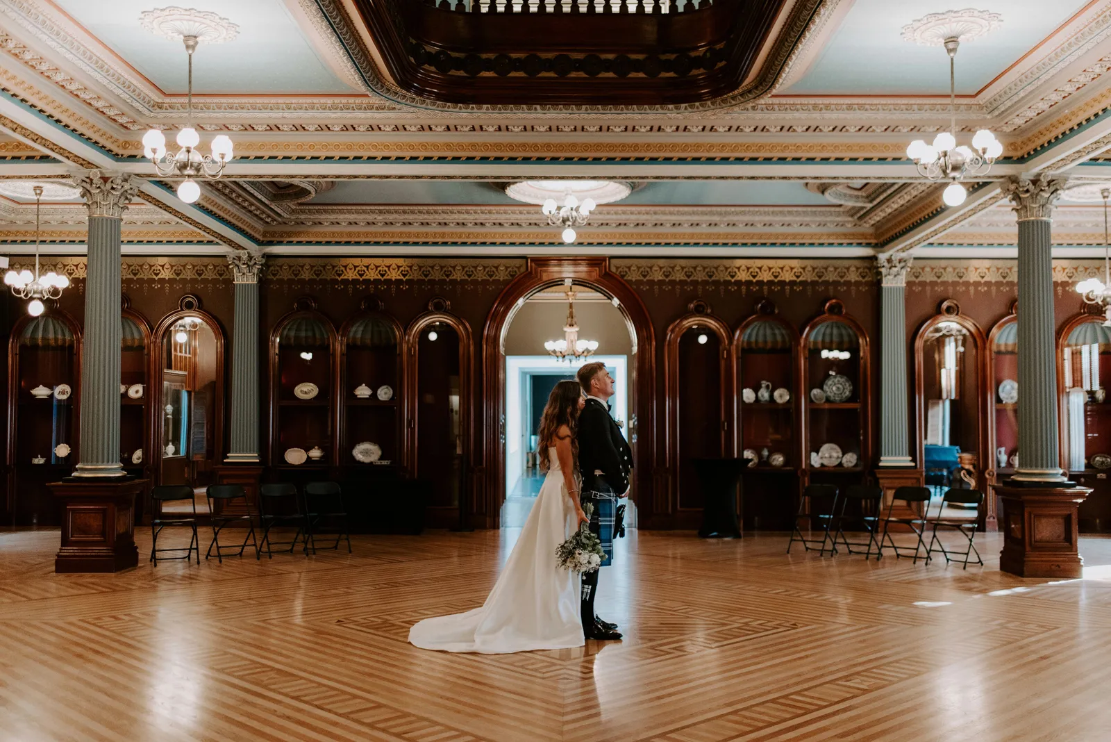 Bride resting her head on her groom's back in a large ballroom.