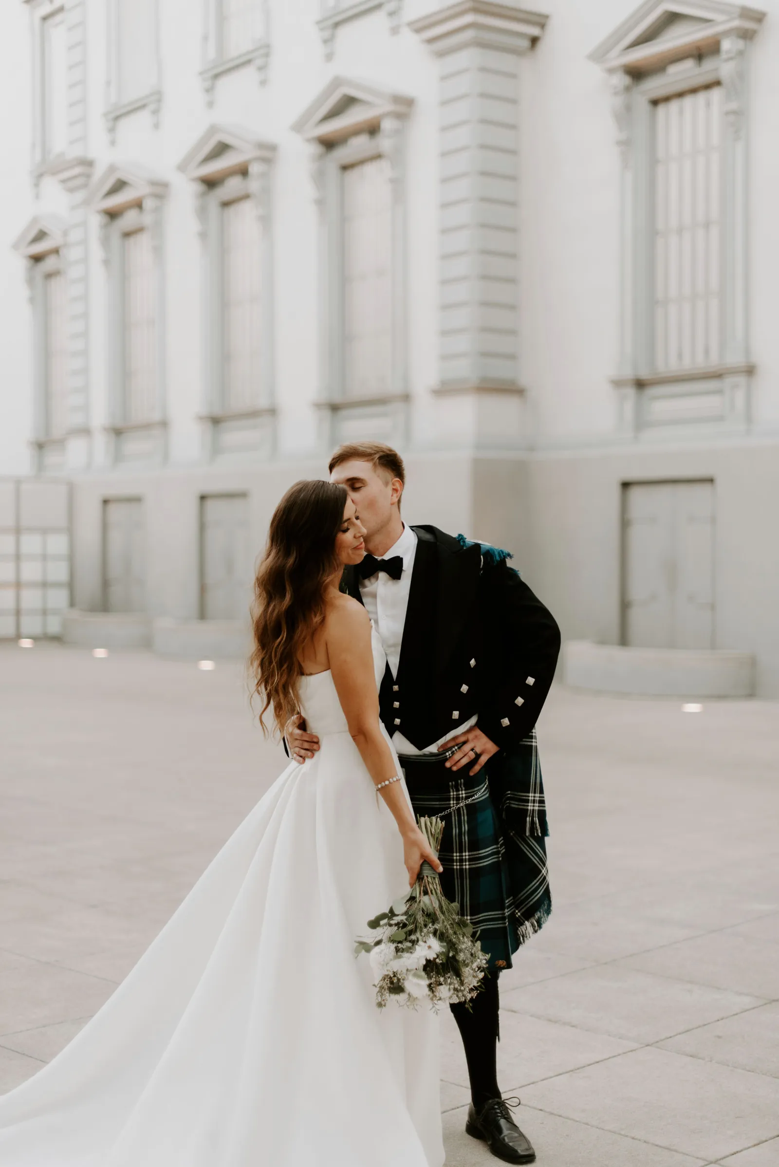 Groom kissing his bride on the forehead outside of the Crocker Art Museum.