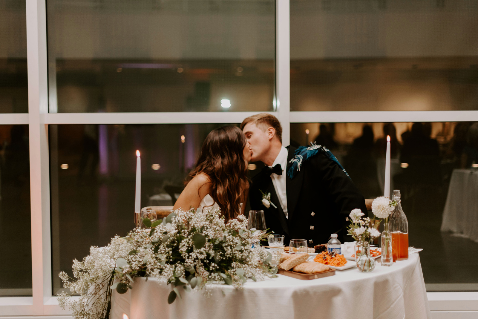 Bride and groom kissing at their table at the reception.