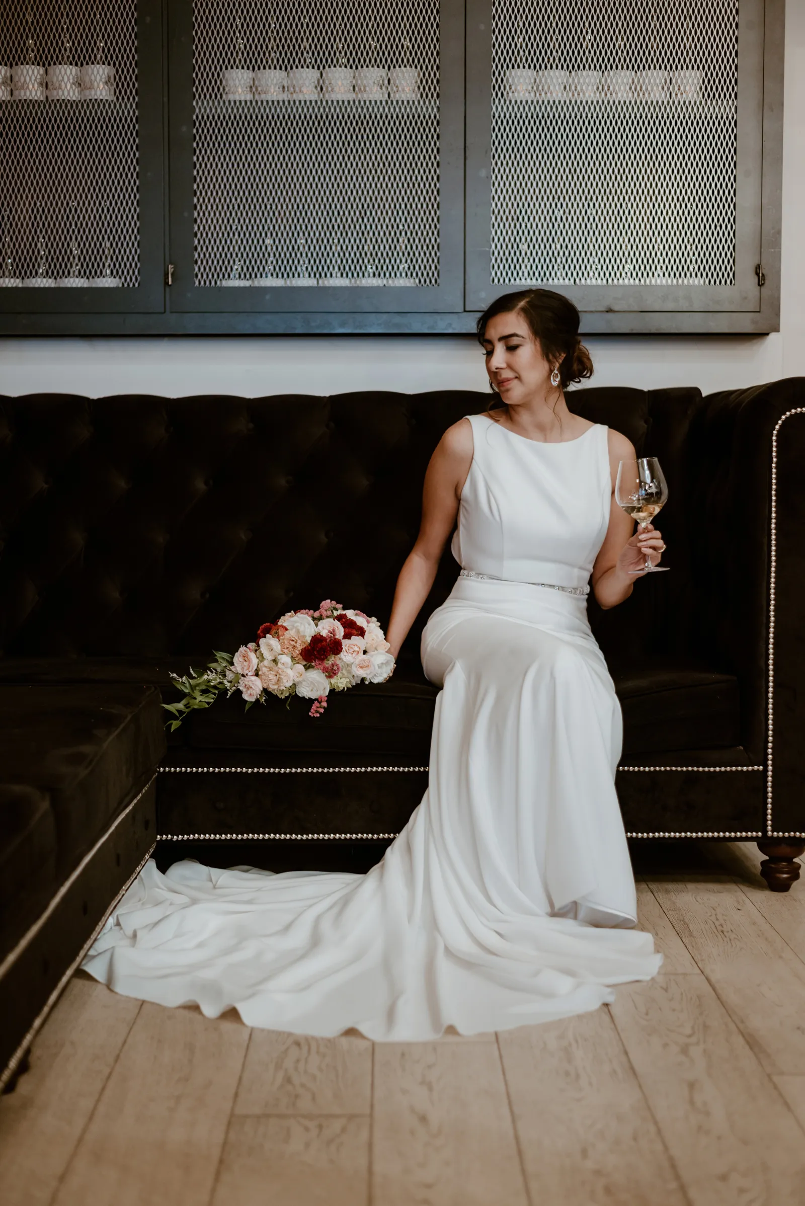 Bride smiling on a couch with a glass of wine.