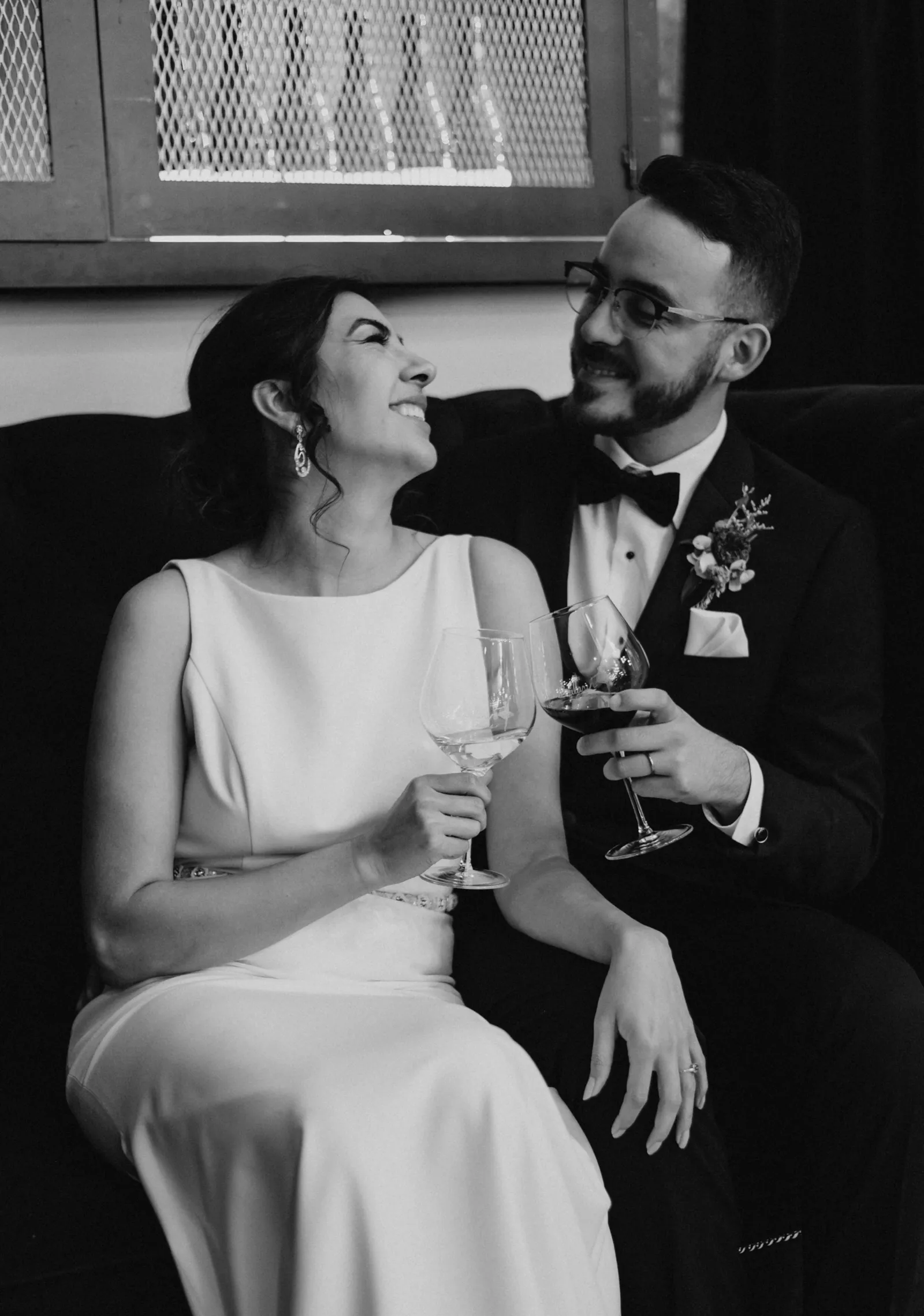 Black and white photo of the bride and groom cheersing and laughing.