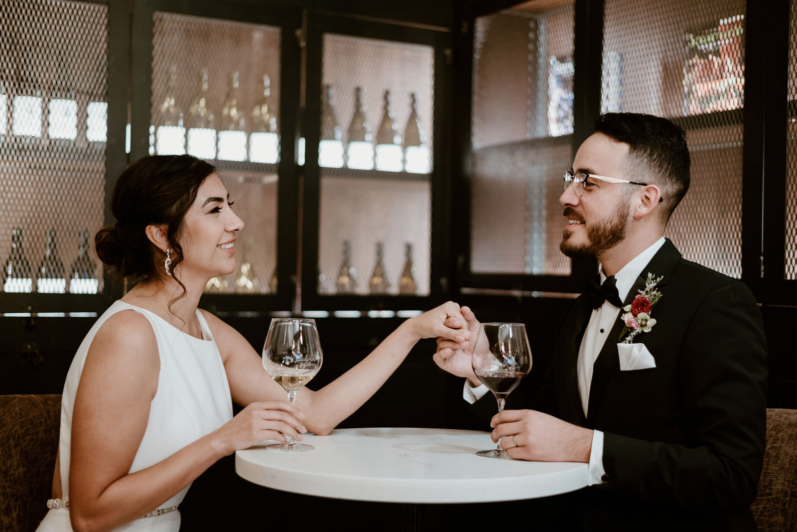 Bride and groom holding hands as they share a glass of wine.