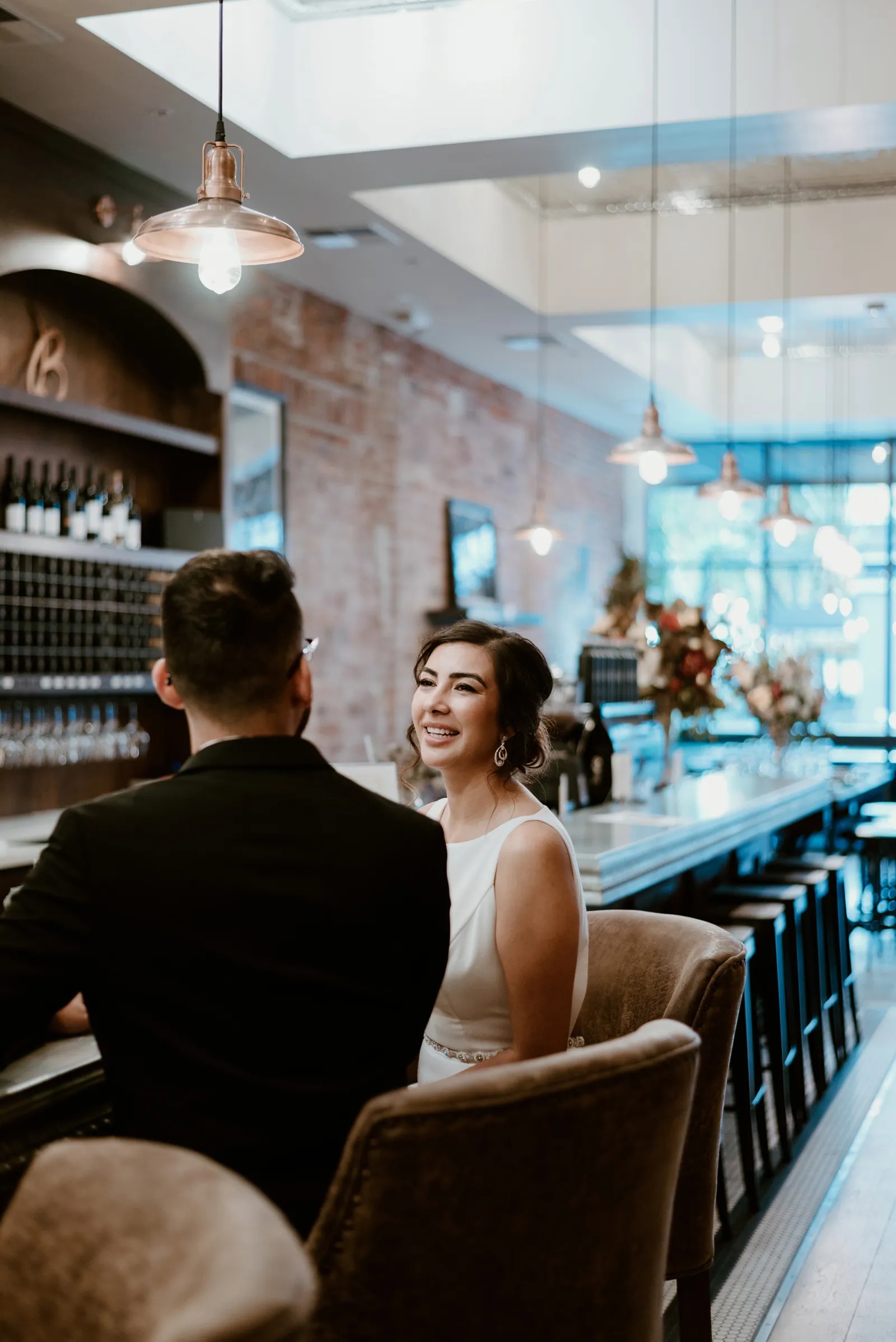 Bride and groom sitting at bar, the groom's back to the camera.