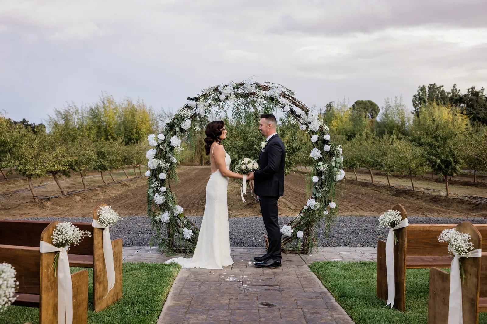 Bride and groom posing in front of a circular altar woven with white flowers and greenery.