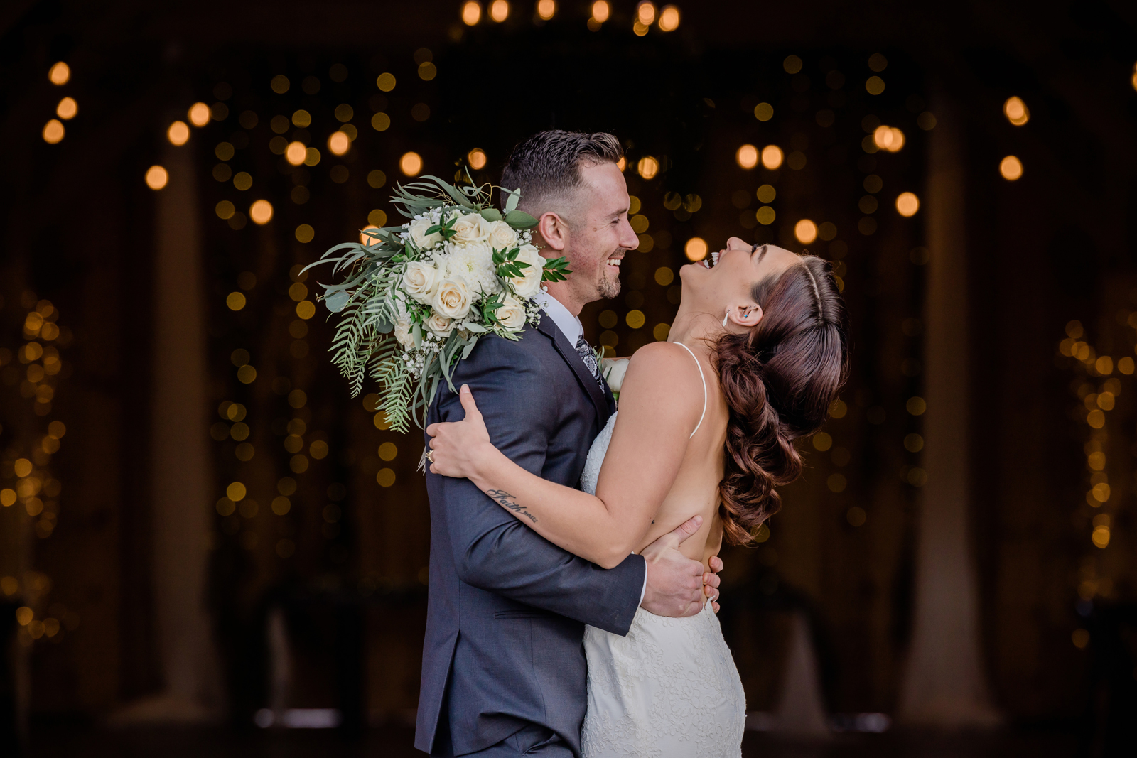 Bride and groom embracing as the bride laughs with her head back.