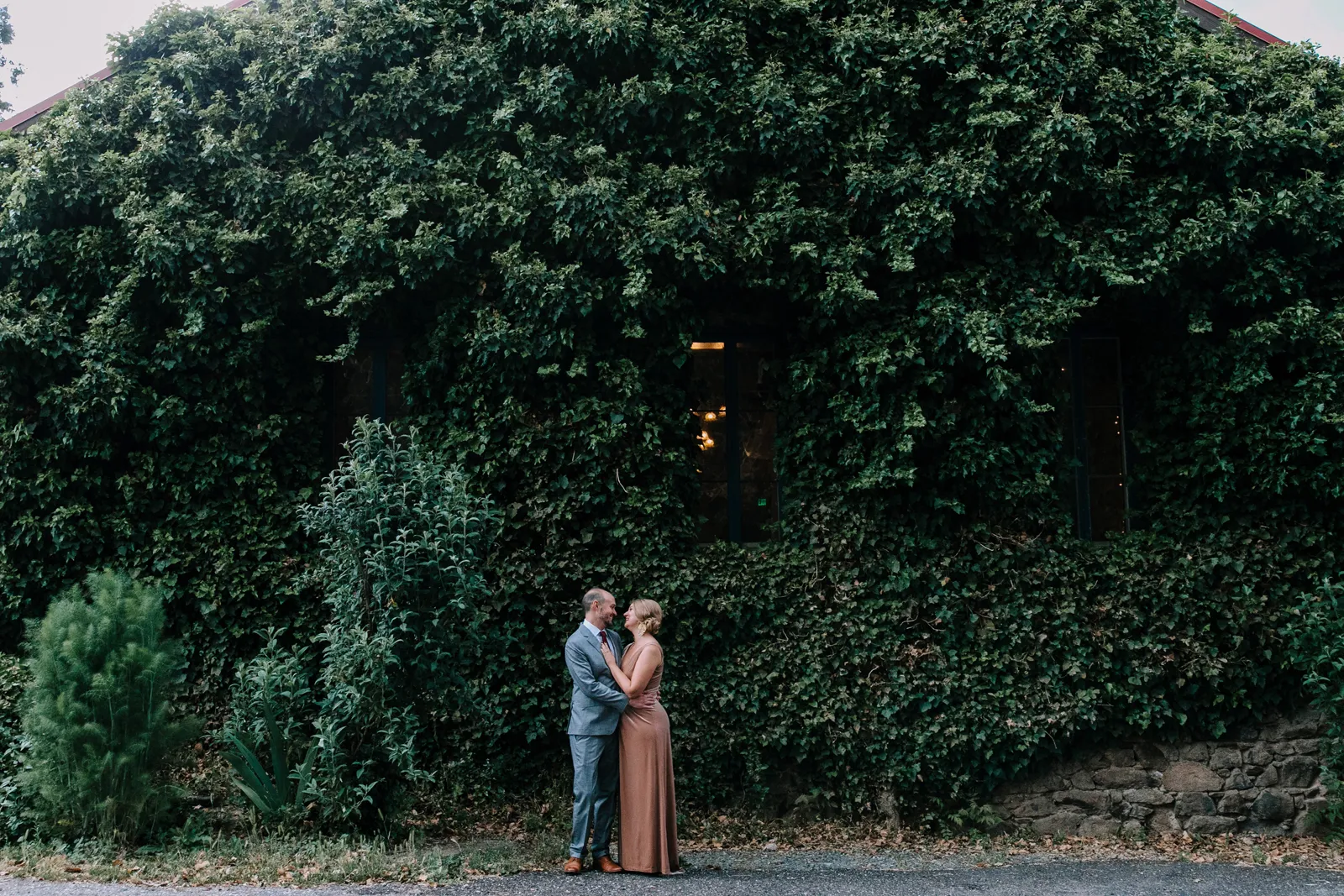 Bride and groom posing in front of a large green shrub.