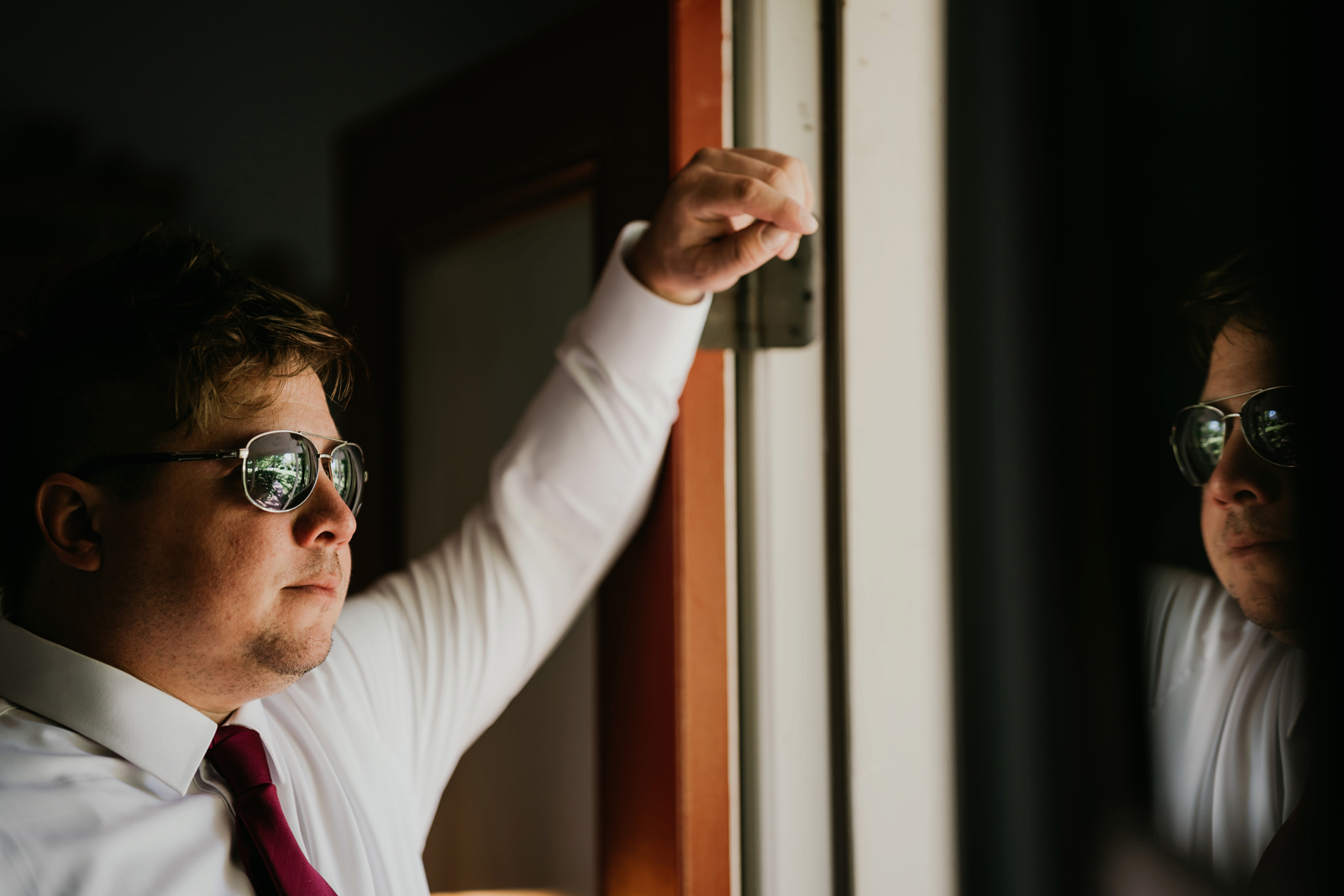 Groom posing and looking out the window with sunglasses on.