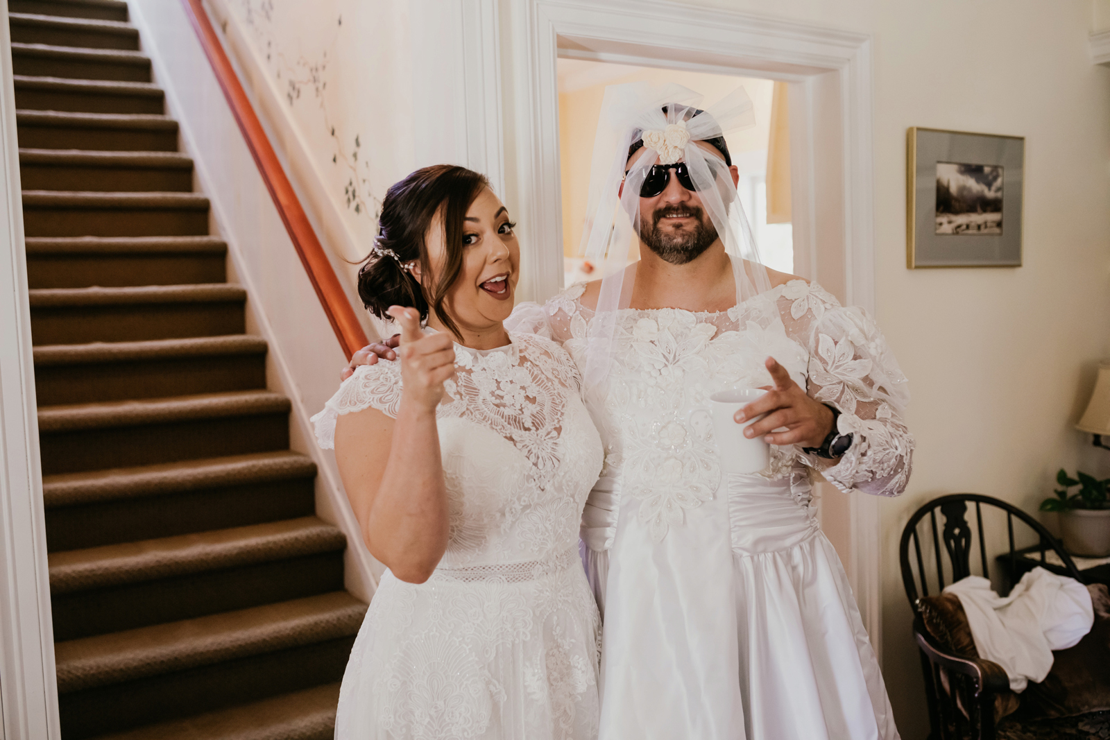 Bride and her friend laughing as he is wearing a fake wedding dress to prank the groom for their first look.