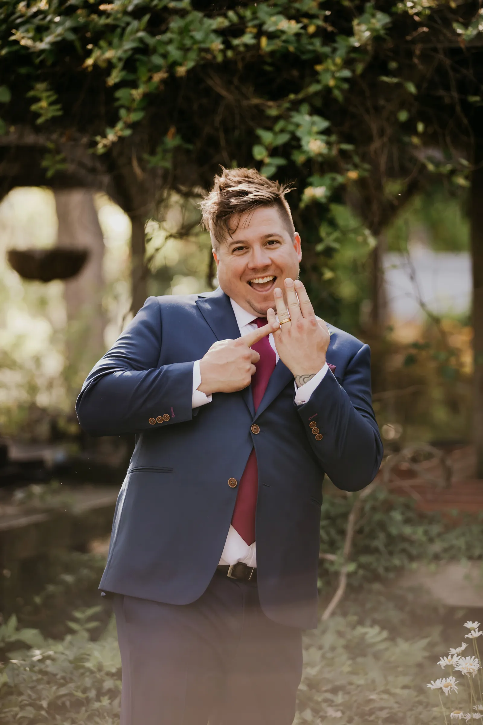 Groom posing and holding up his ring finger to the camera.