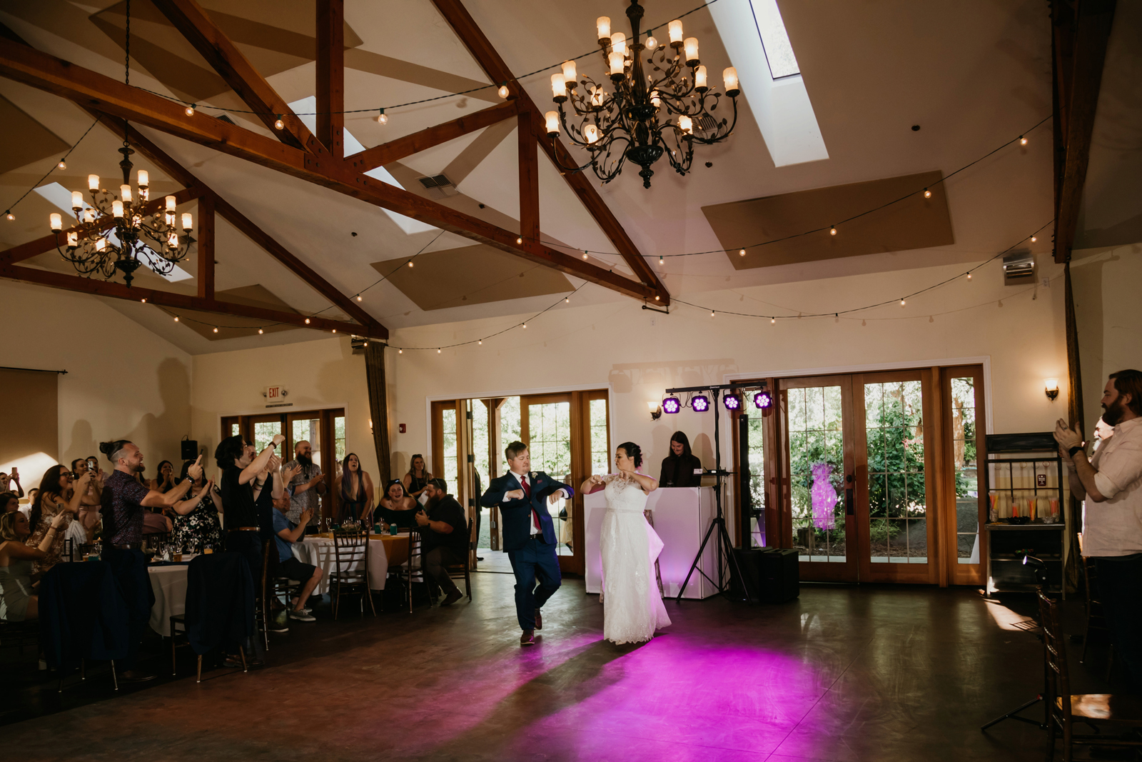 Bride and groom walking into the reception venue holding hands and cheering.