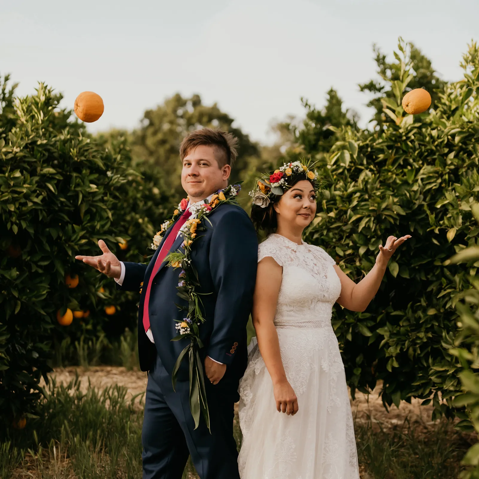 Bride and groom tossing up some oranges and smiling at the camera.