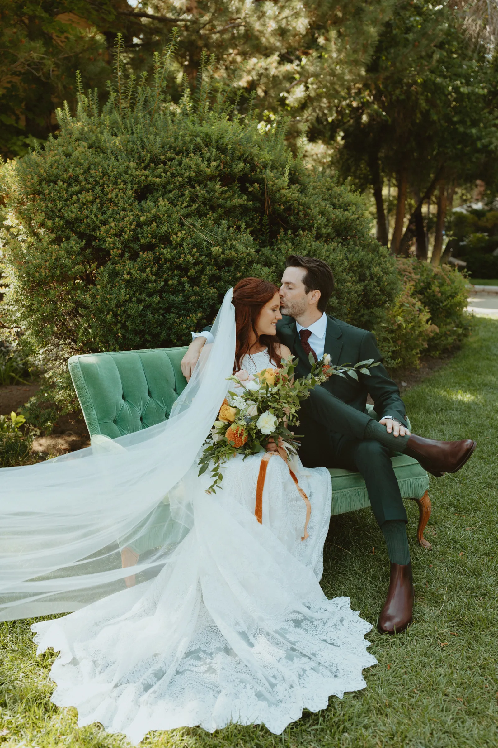 Bride and groom sitting on a couch outside and posing for photos.