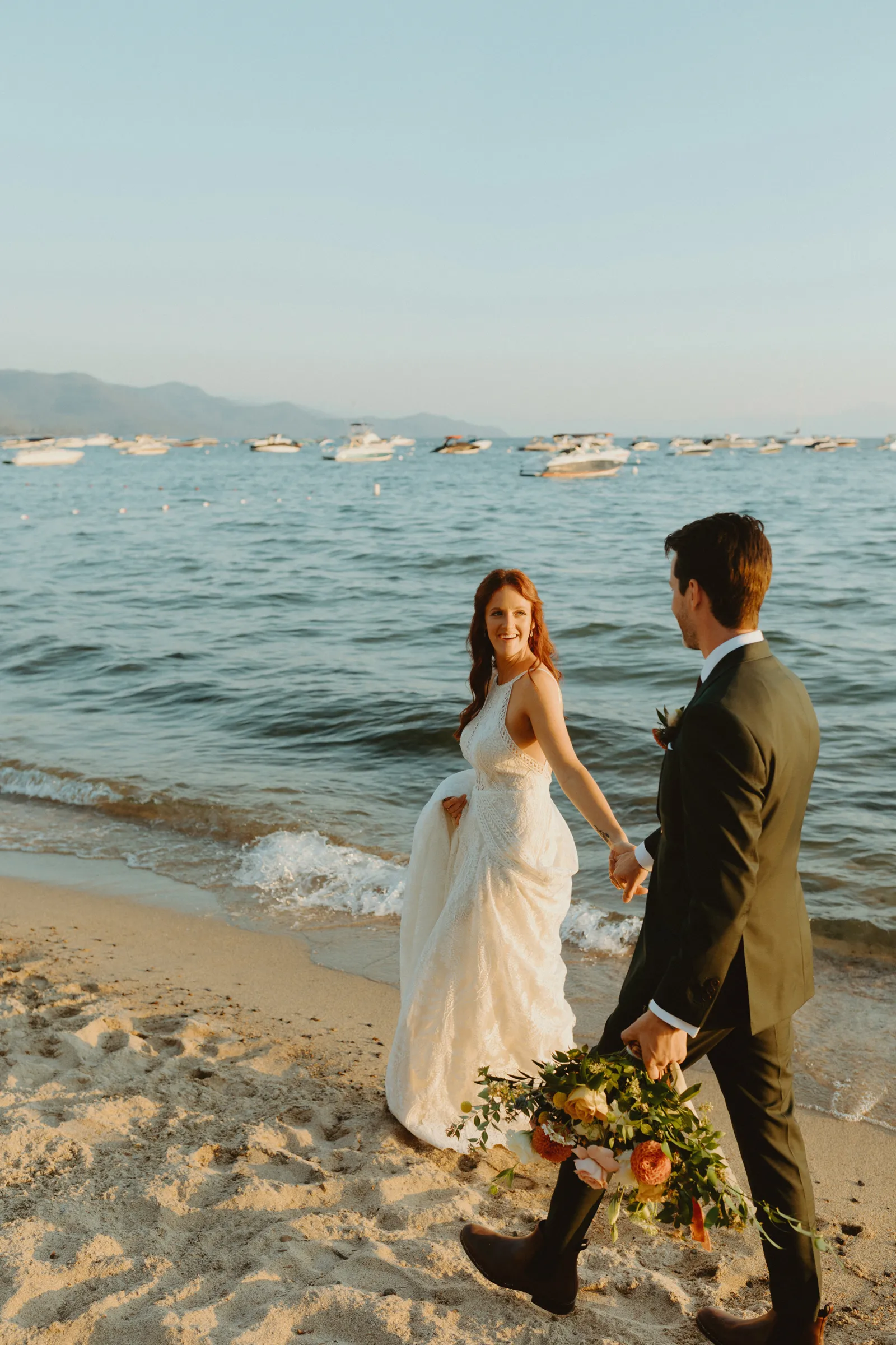 Bride reaching for her husband's hand on the beach.