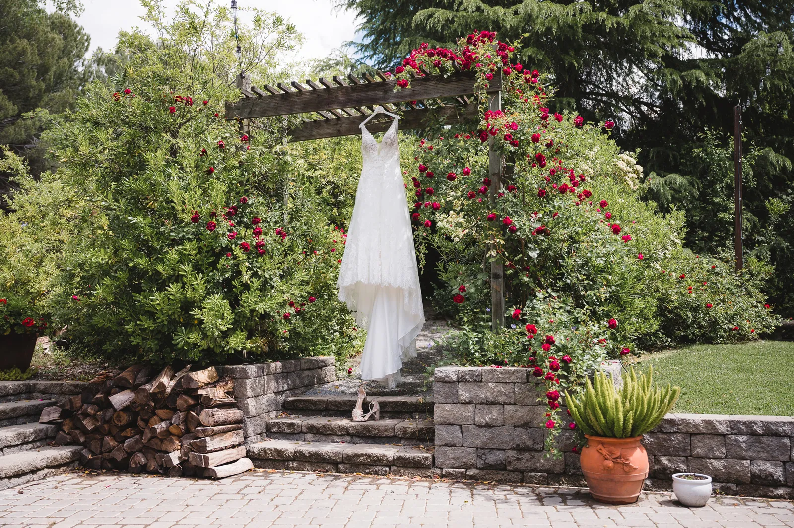 Photo of a wedding gown hanging outside on an arch with flowers.