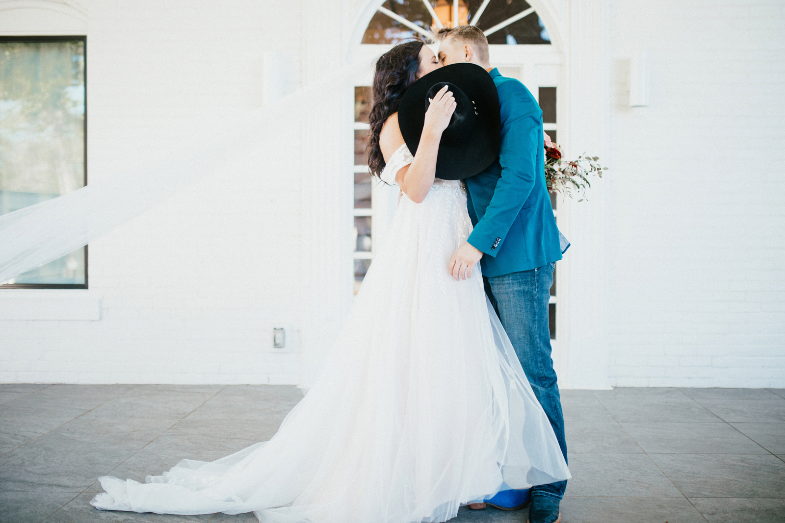 Bride and groom kissing behind a black cowboy hat.