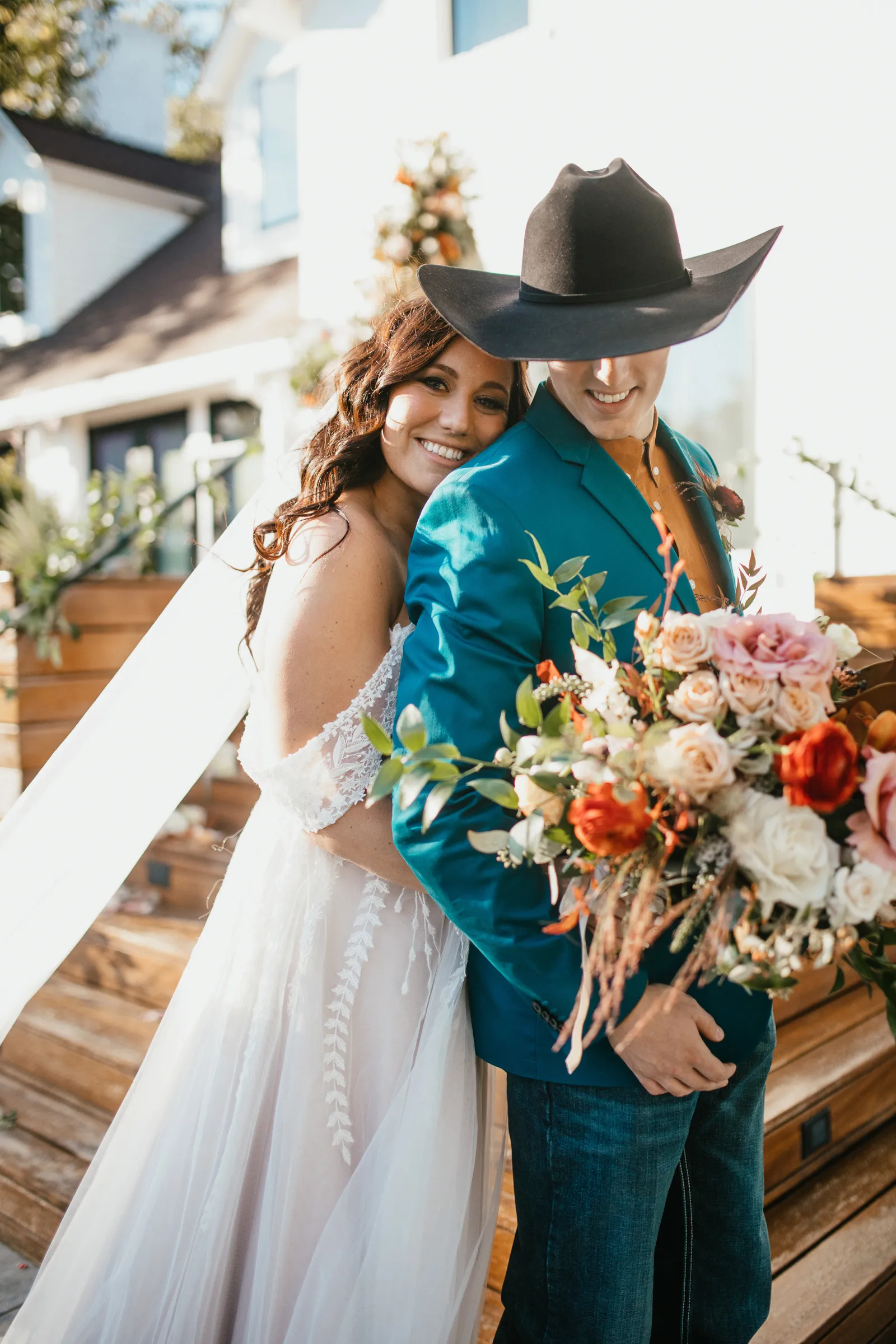 Bride hugging her groom from behind and smiling at the camera.