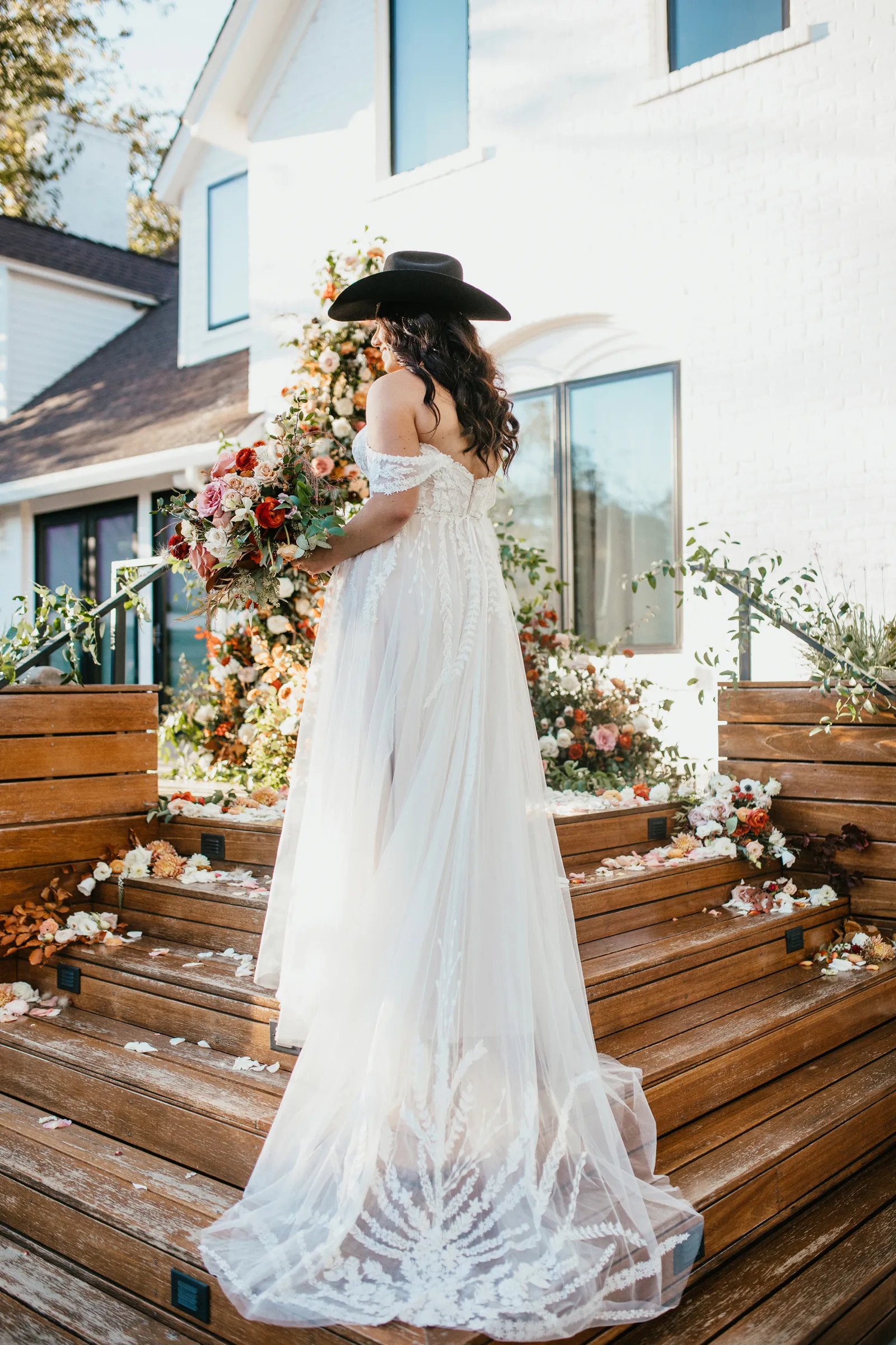 Bride posing on the stairs, laughing with her black cowgirl hat on.