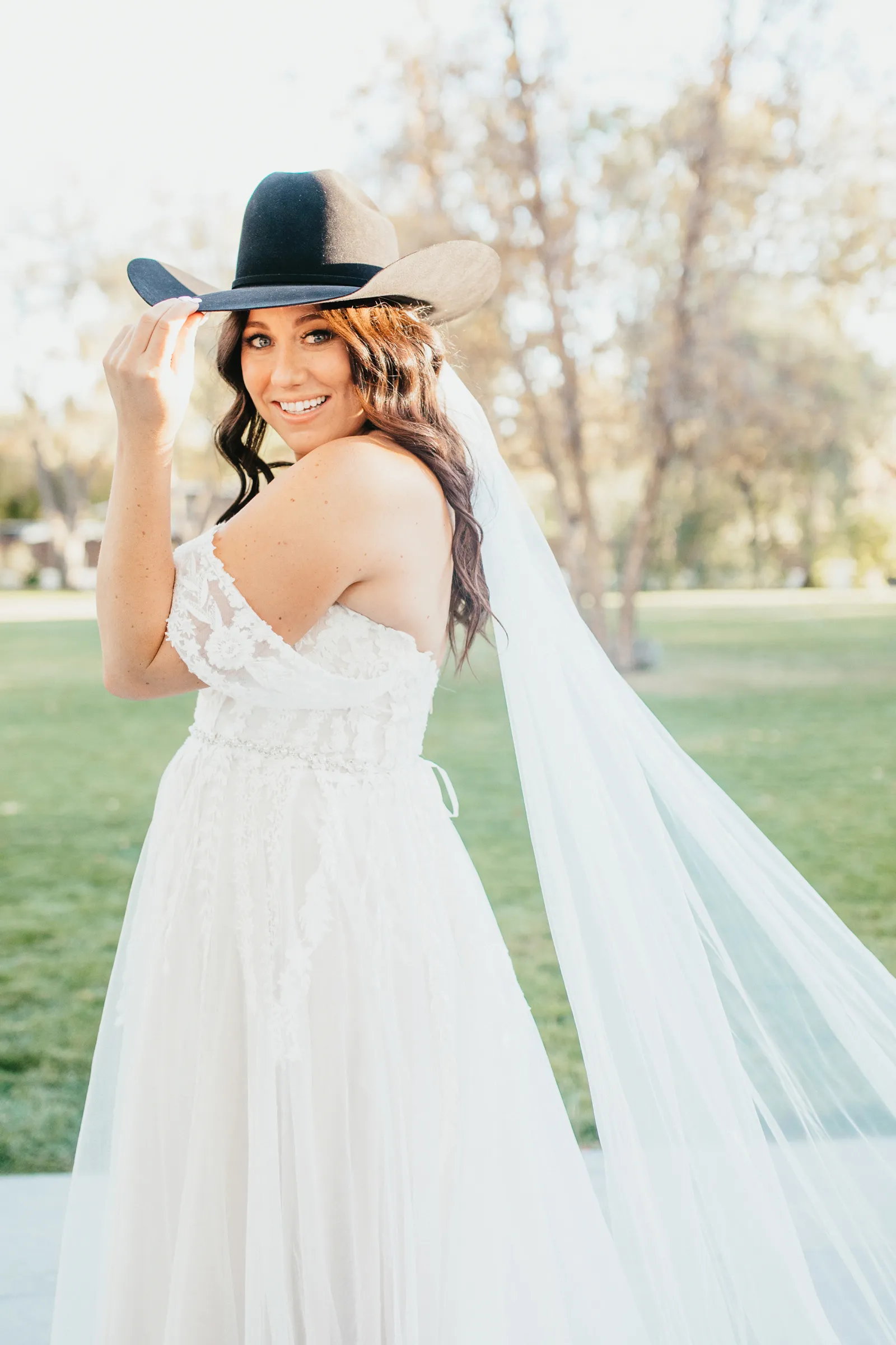 Bride tilting her cowgirl hat to the camera and smiling.