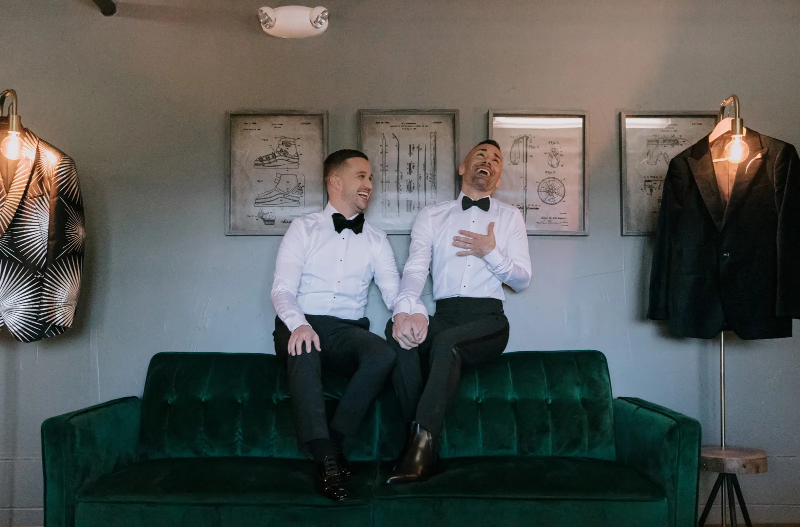 Two grooms sitting on a green couch, getting ready for their rustic-chic wedding.