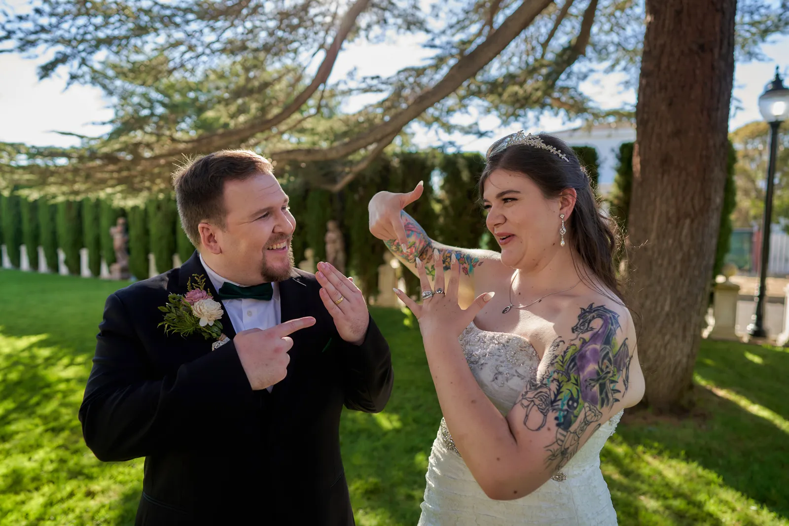 Bride and groom pointing to their ring fingers.