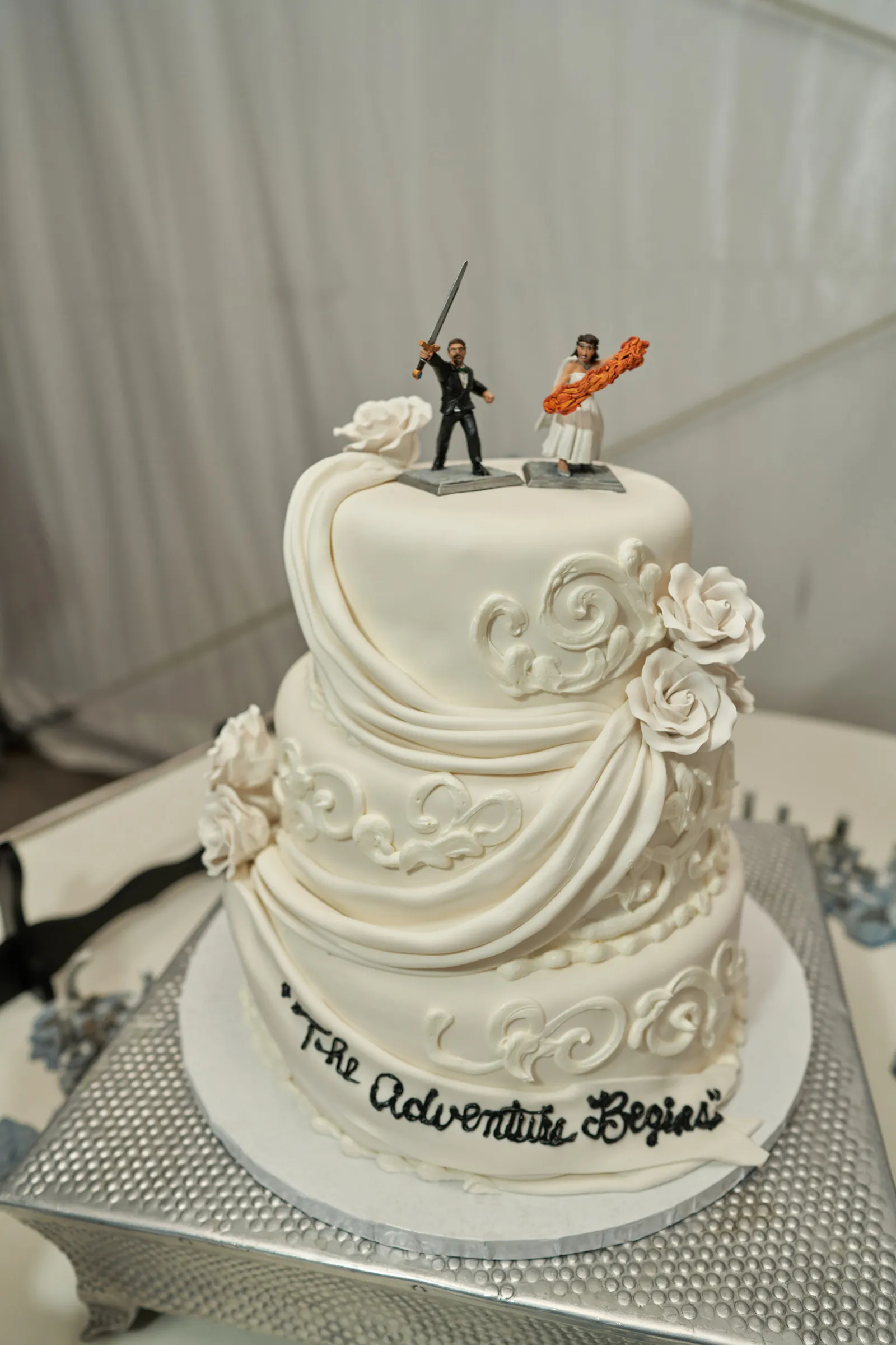 White wedding cake with two figurines on top with swords and a lightsaber.