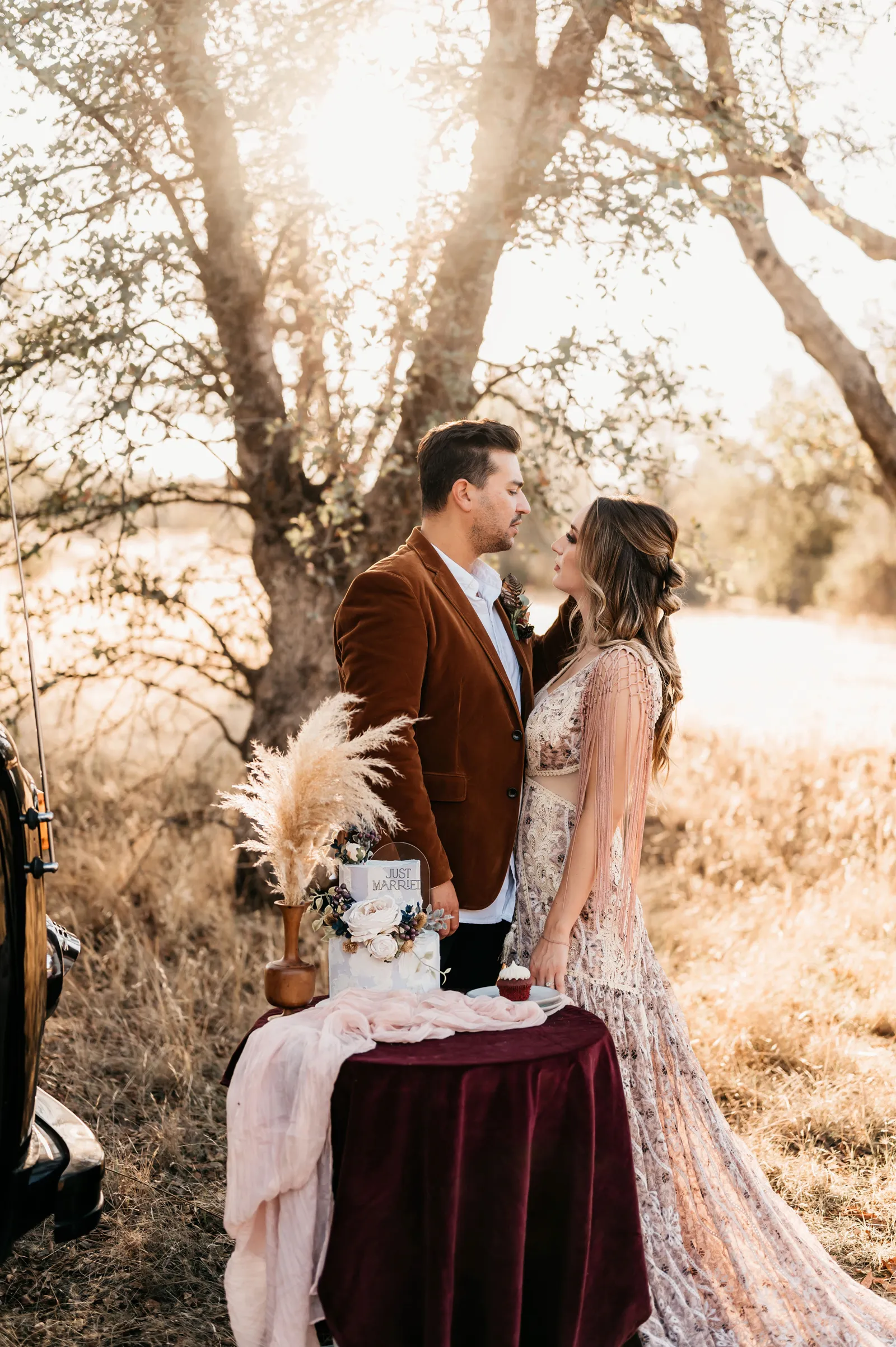 Bride and groom smiling at each other by their eclectic boho wedding cake.