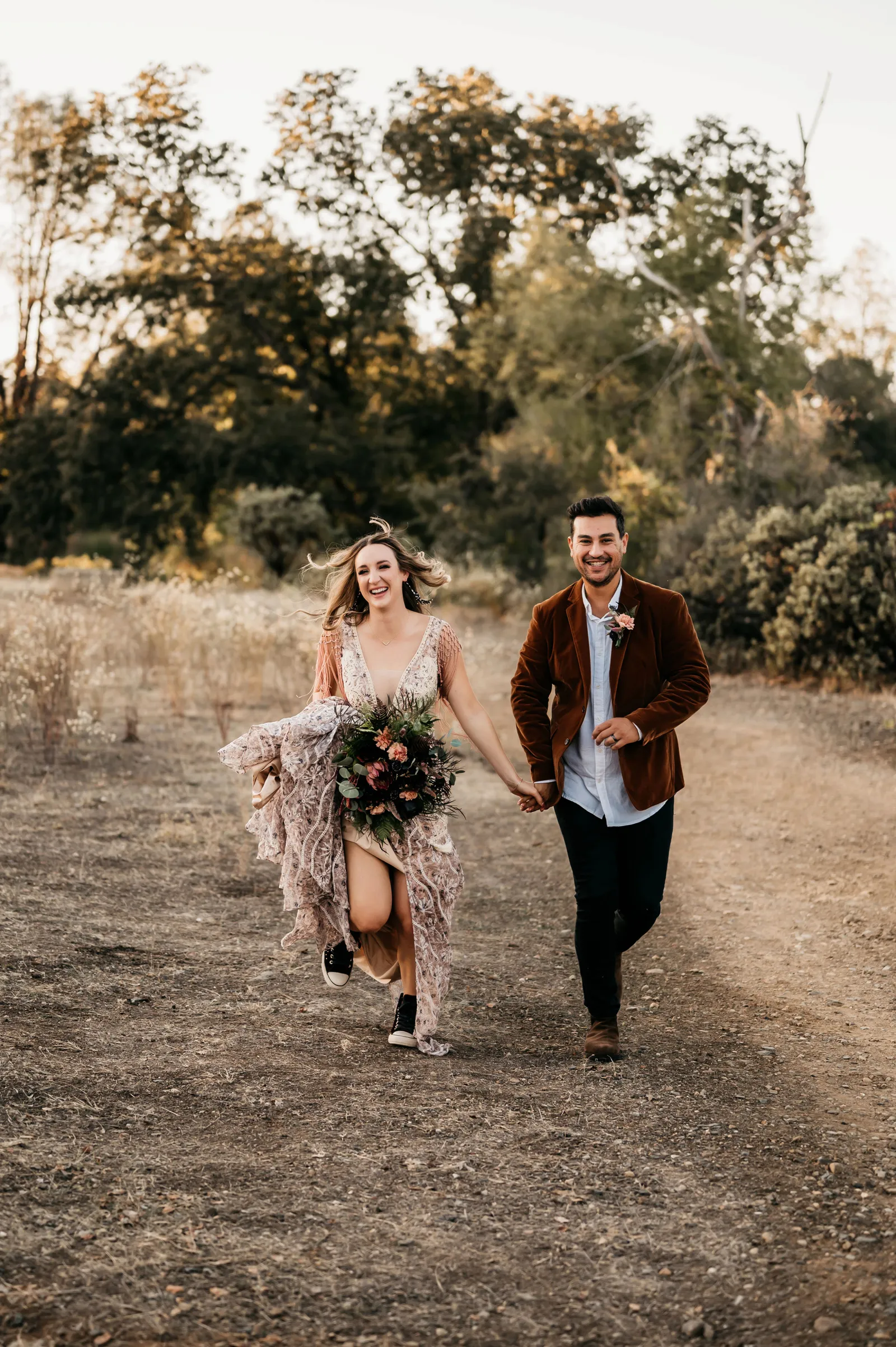 Bride and groom running through a field together and laughing.