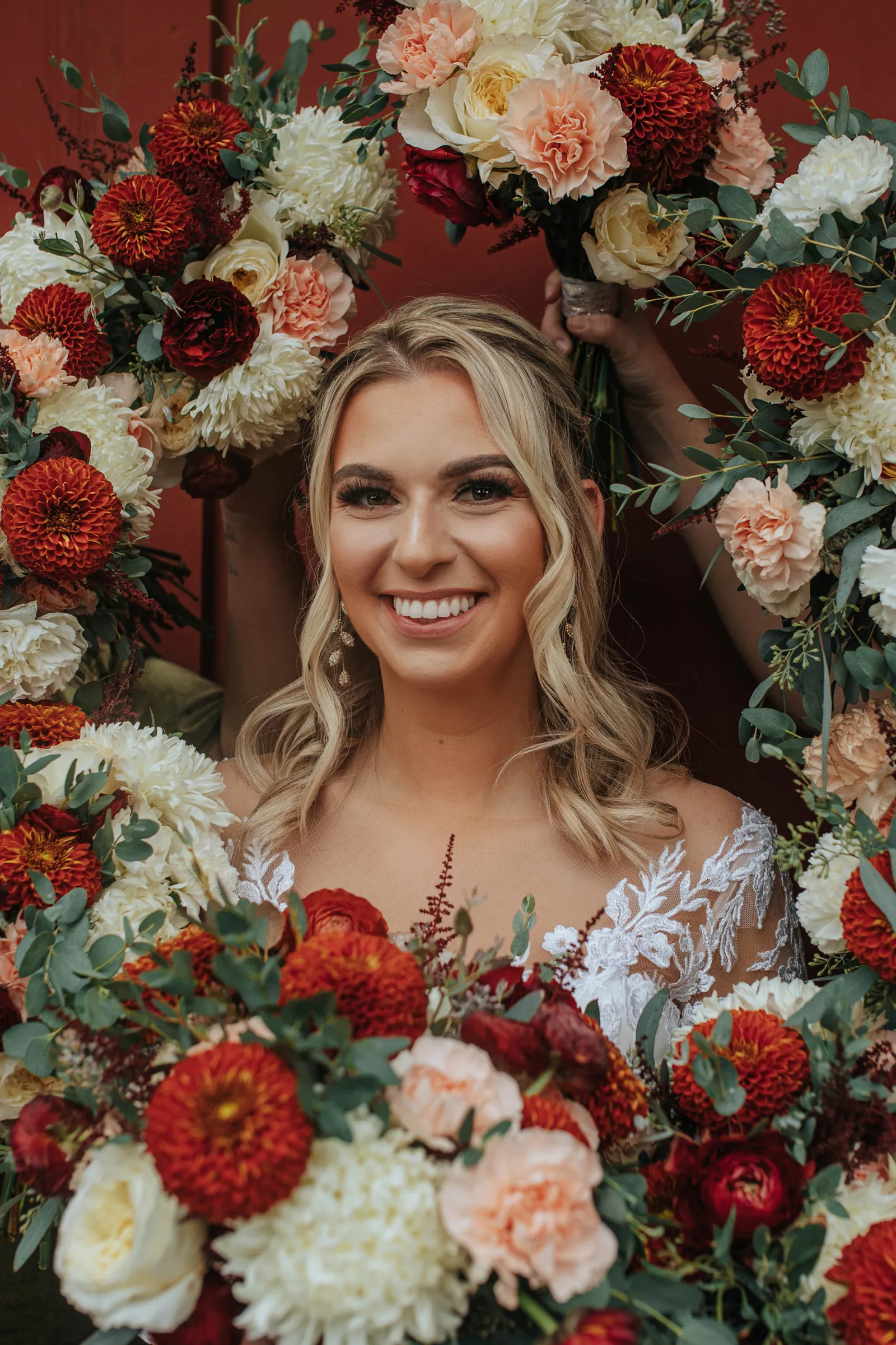 The bride surrounded by white and red florals at her red barn wedding ceremony.