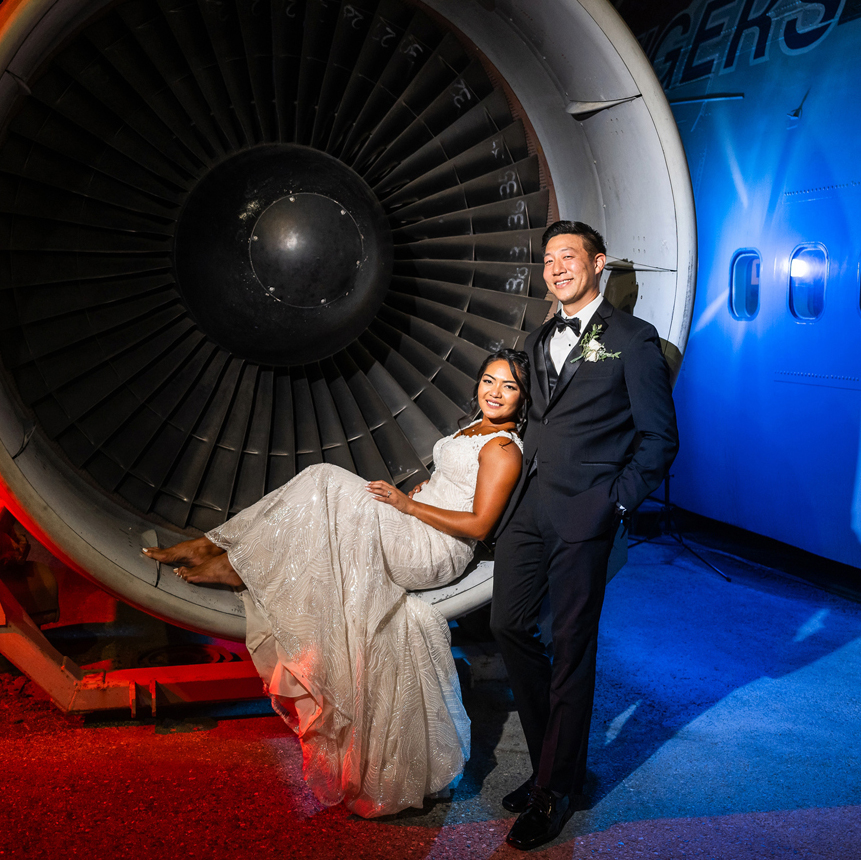 Newlyweds posing in the engine of an airplane at their elegant aviation museum wedding.