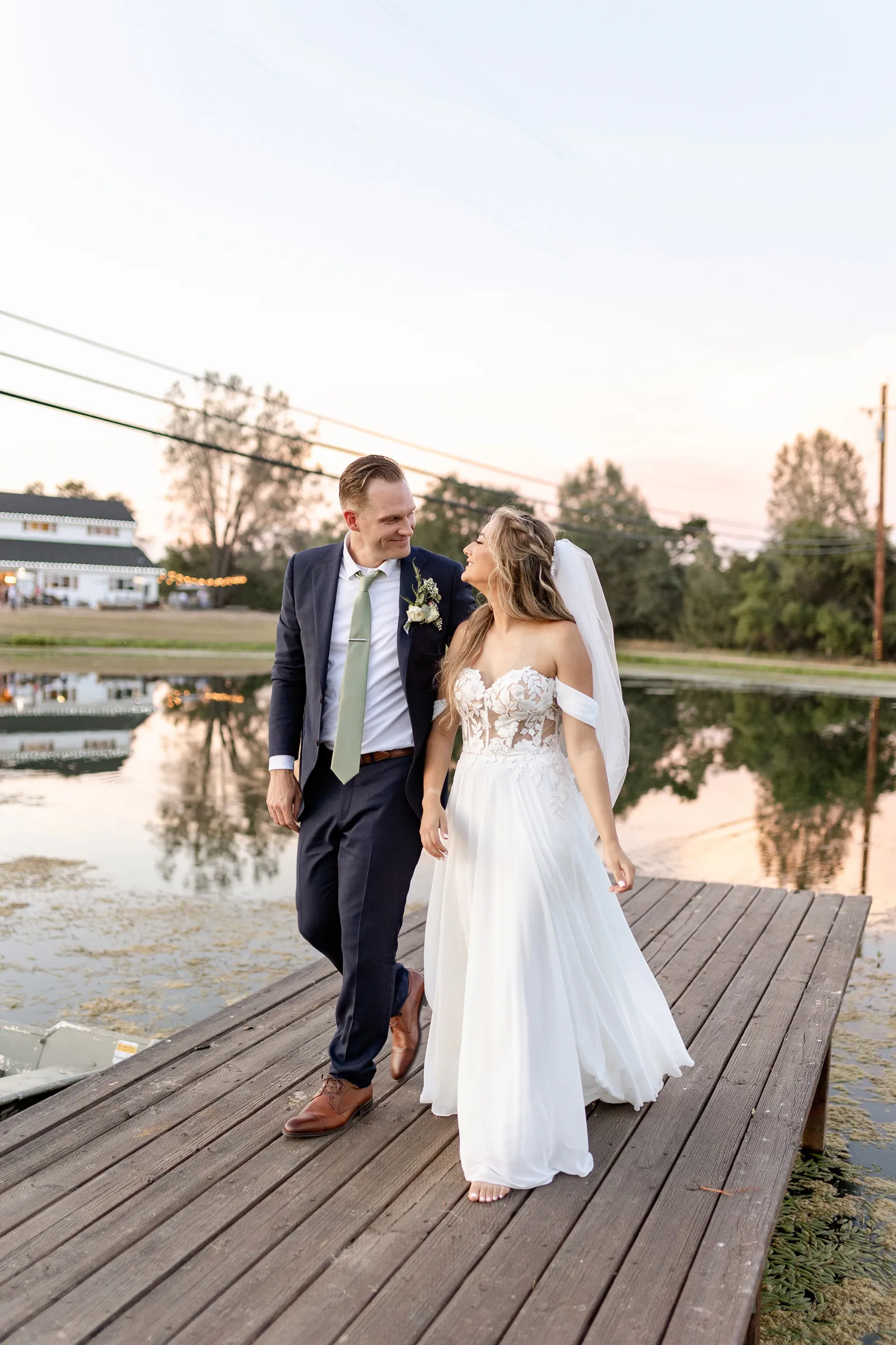 Newlyweds walking together on a small pier at their elegant outdoor wedding.